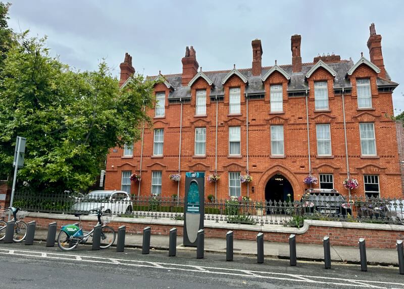 Red brick hotel with many chimneys and gabled windows on a tree-lined street.