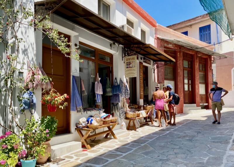 Pedestrians peer in the doorway of a small shop selling hand-woven goods in a Greek village.