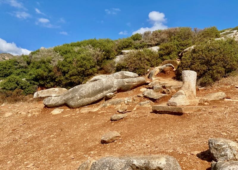 Human-shaped statue, fallen to the ground and broken in the dark red soil.