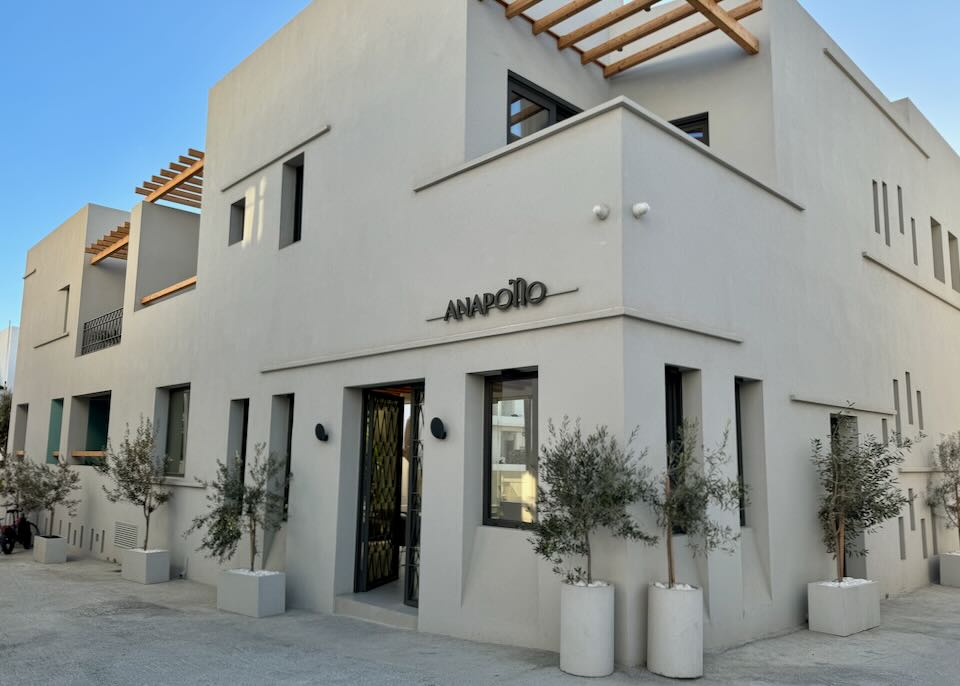 Small, boxy, sand-colored Cycladic hotel against a blue sky.