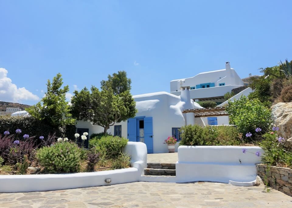 White Cycladic-style hotel next to green trees and a blue sky