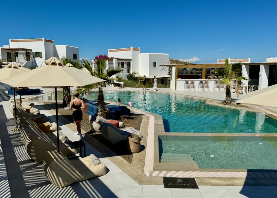 Hotel swimming pool surrounded by boxy white buildings.