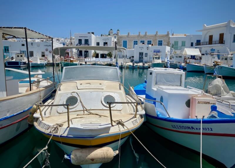 Boats moored in a small harbor ringed by boxy white buildings. 