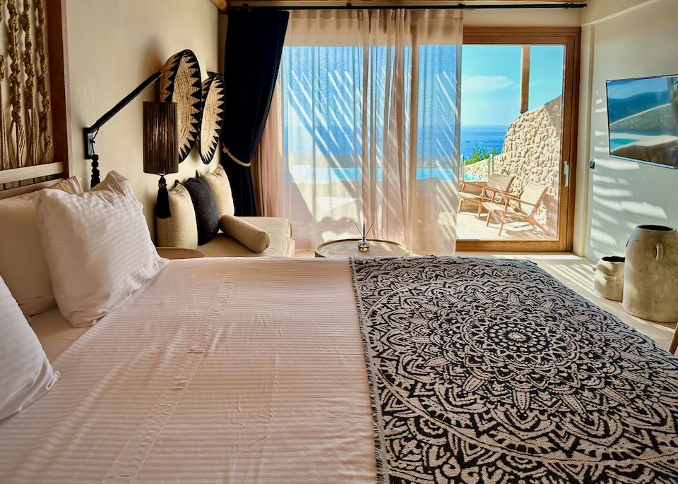 Beautifully dressed bed in a luxury boho-chic hotel room next to an open balcony door