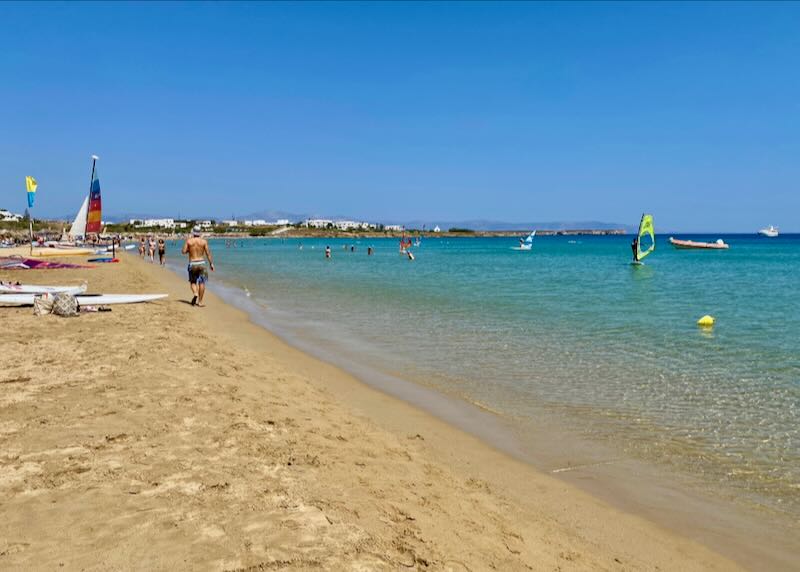 A man walks down a wide beach with golden sand