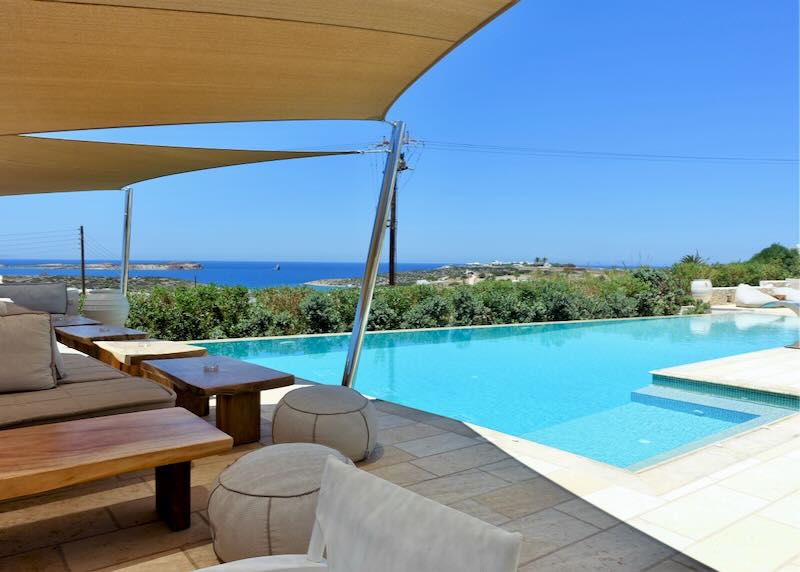 Sun beds shaded by triangular sails, next to a blue swimming pool