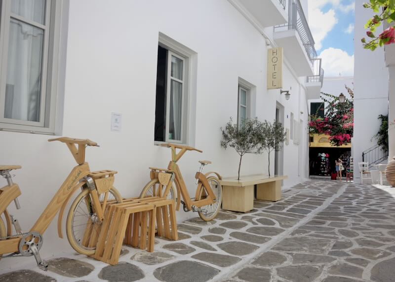 View looking down a narrow white alley in a Greek village past a hotel doorway with bamboo bicycles parked in front