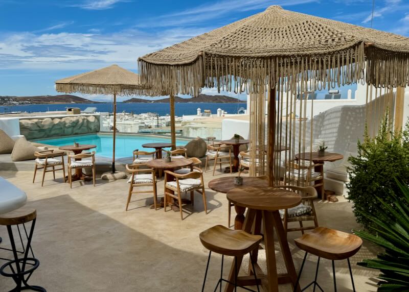 Small boho-chic hotel swim deck with umbrella covered tables. 