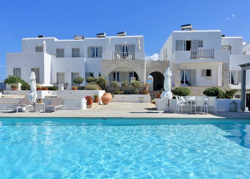 White, cycladic-style hotel, as seen across a sparkling blue swimming pool on a sunny day