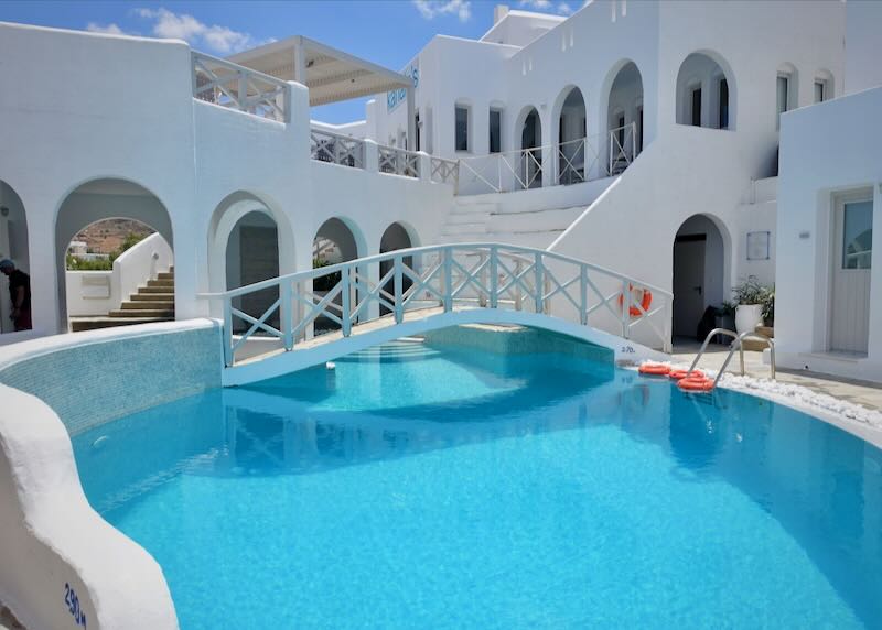 Blue swimming pool surrounded by white buildings with arched doorways 