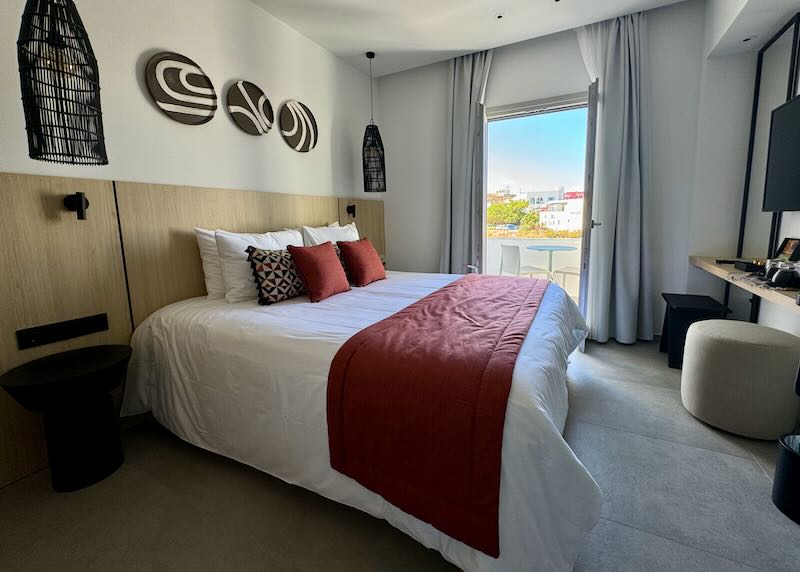 Luxury hotel room with open balcony doors showing a Greek village beyond