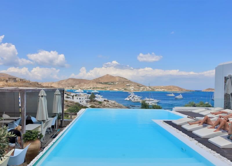 View looking over a hotel swimming pool to the blue sea and distant green hills