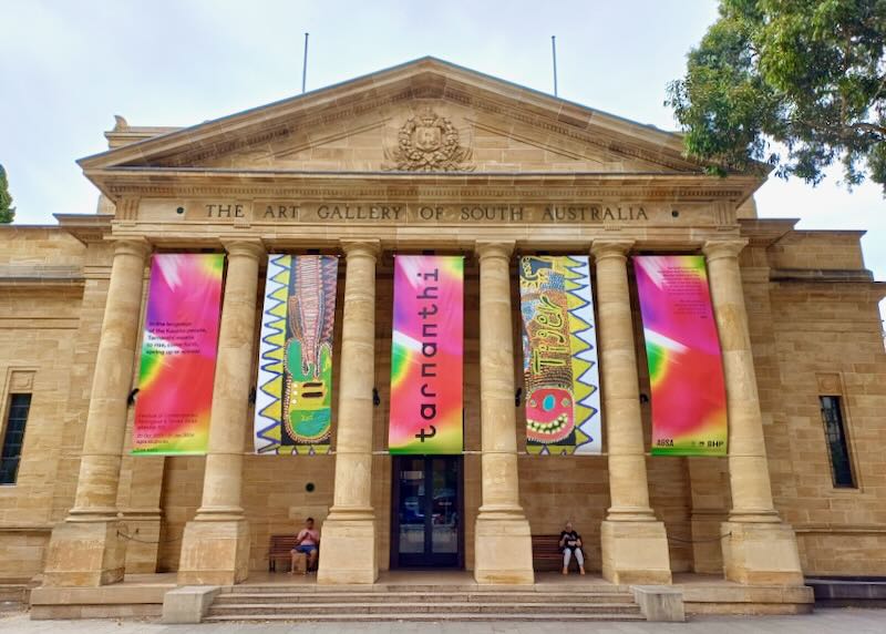 Bright pink, yellow, and green banners hang out side an art museum.