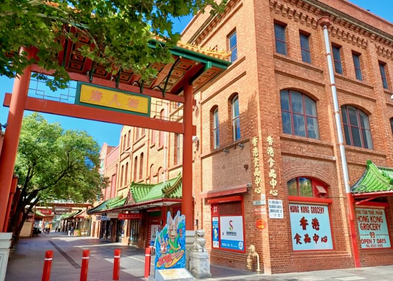 A red brick building with a red, green, and yellow Chinese arch into Chinatown.