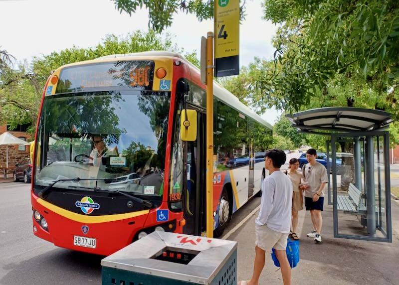 People stand at a bus stop and wait for the bus to arrive.