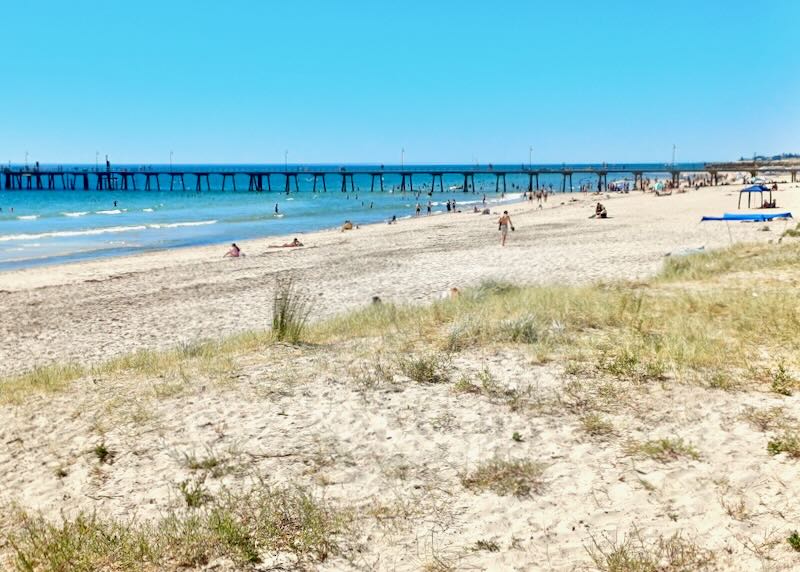 People walk along a beach by a pier.