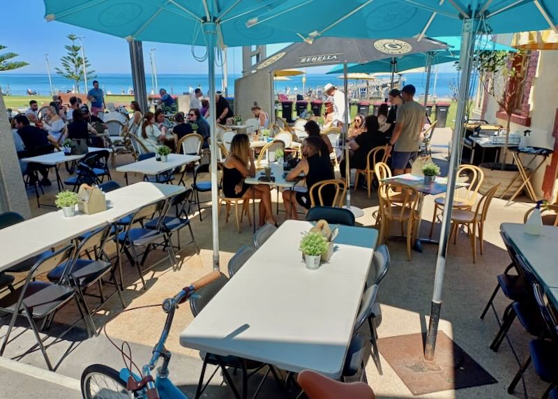 People sit at tables by the ocean.