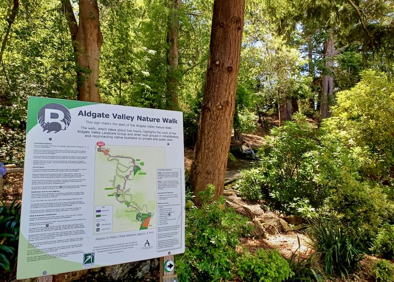 A sign before a hiking path through the woods.