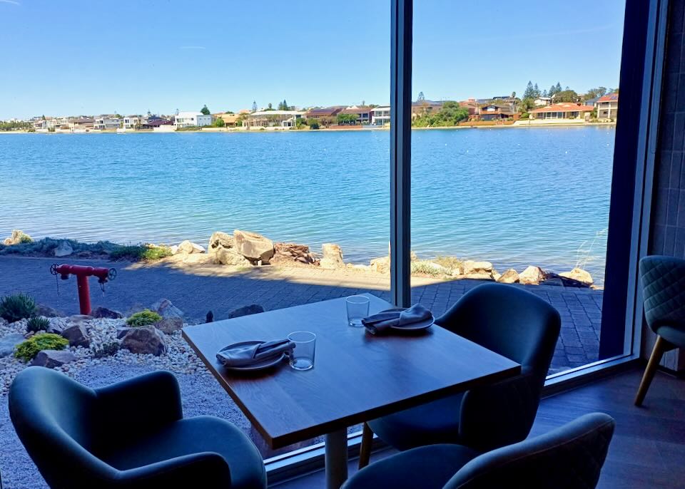 A table sits in a restaurant next to a full length window with views of a blue lake.