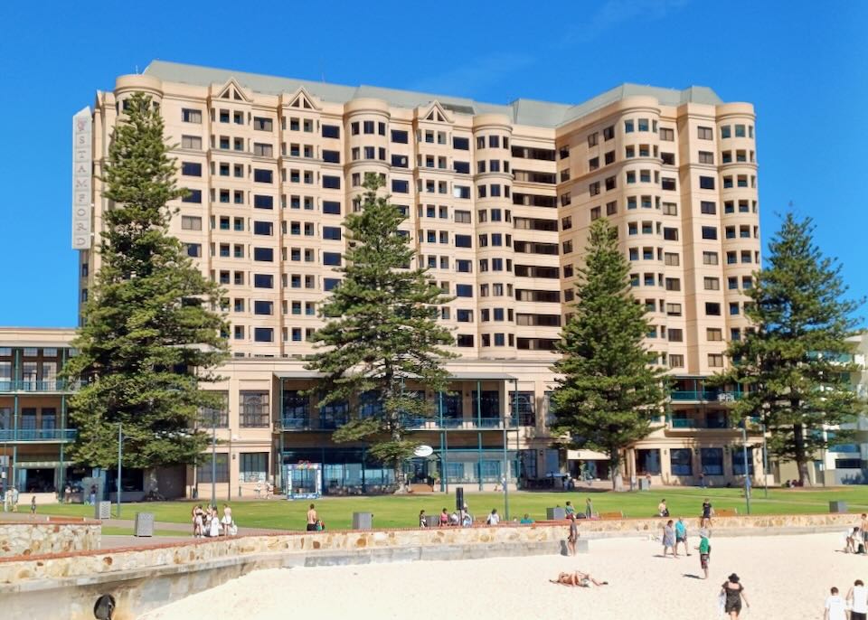 A tall hotel with tan stone stands over the sand and ocean.