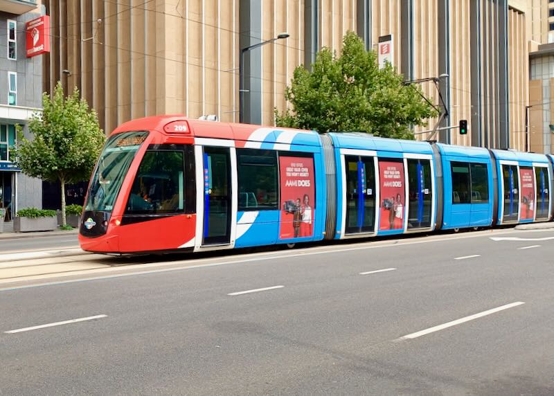 A red and blue tram glides on the streets of downtown.