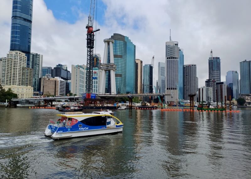 A blue and white ferry boat rides on the river next to the downtown high rises.