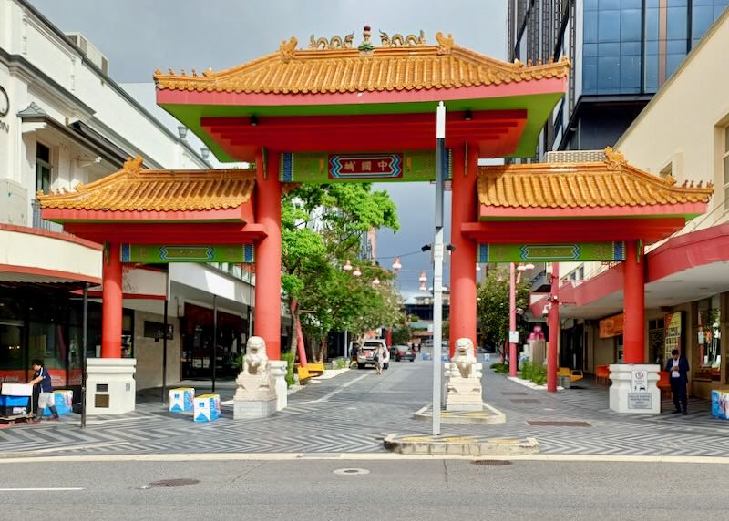 A tall large red square gate with a gold top sits at the entrance of Chinatown.