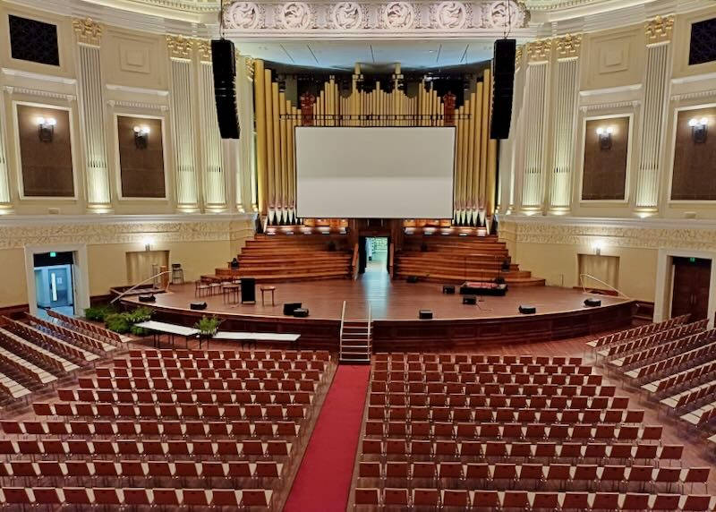 A theater with red seats and wood stage with organ pipes and relief wall sculptures.