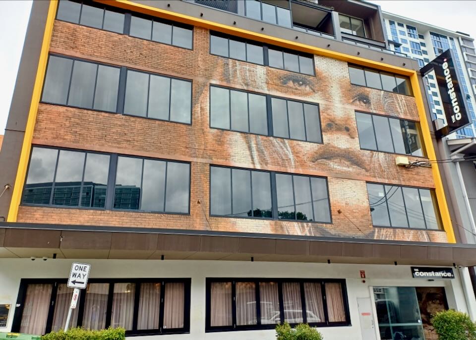 On the outside of a small brick hotel is a woman's face painted on the brick between the windows.