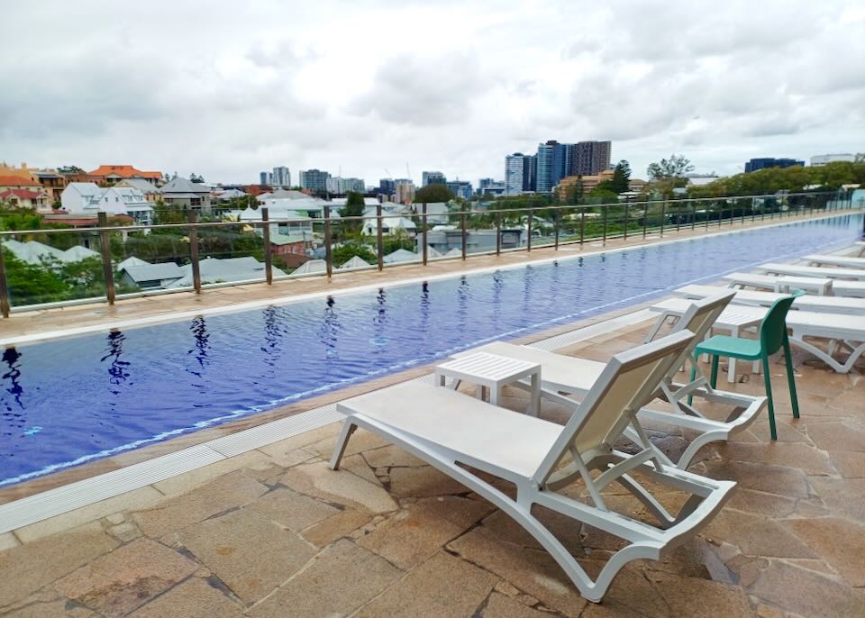 Lounge chairs sit by a thin long rooftop pool under gray skies.