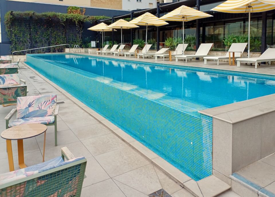 A long small pool with lounge chairs and yellow and white umbrellas.