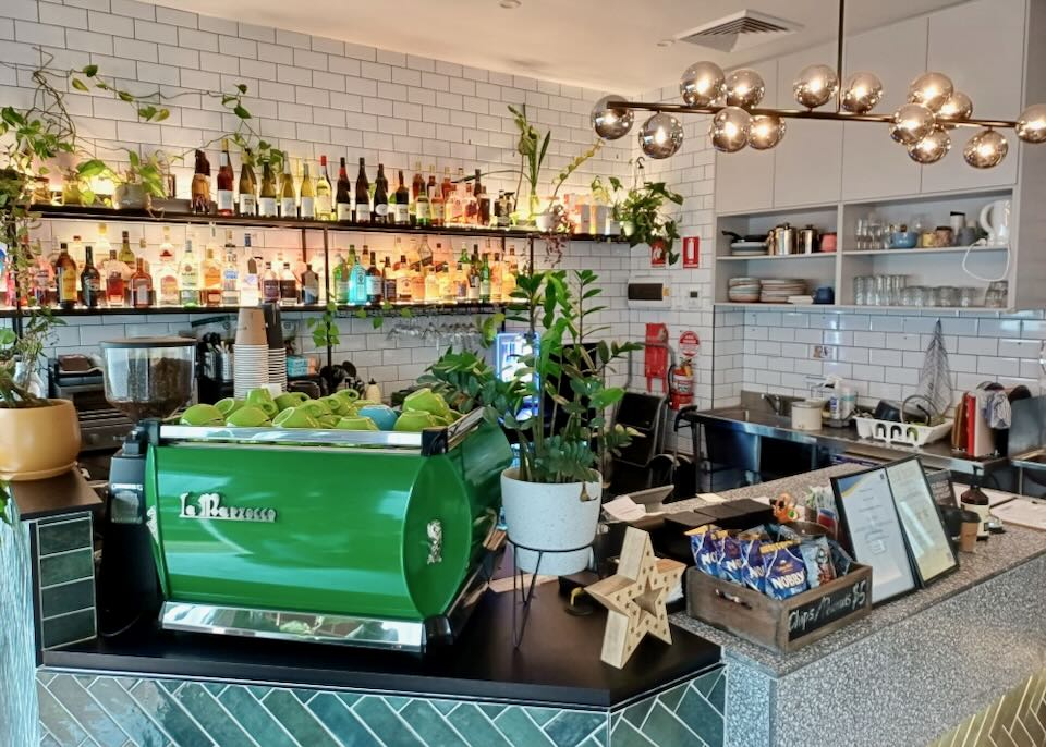 A bright green expresso machine sits on a counter at a brightly lit coffee shop and bar.