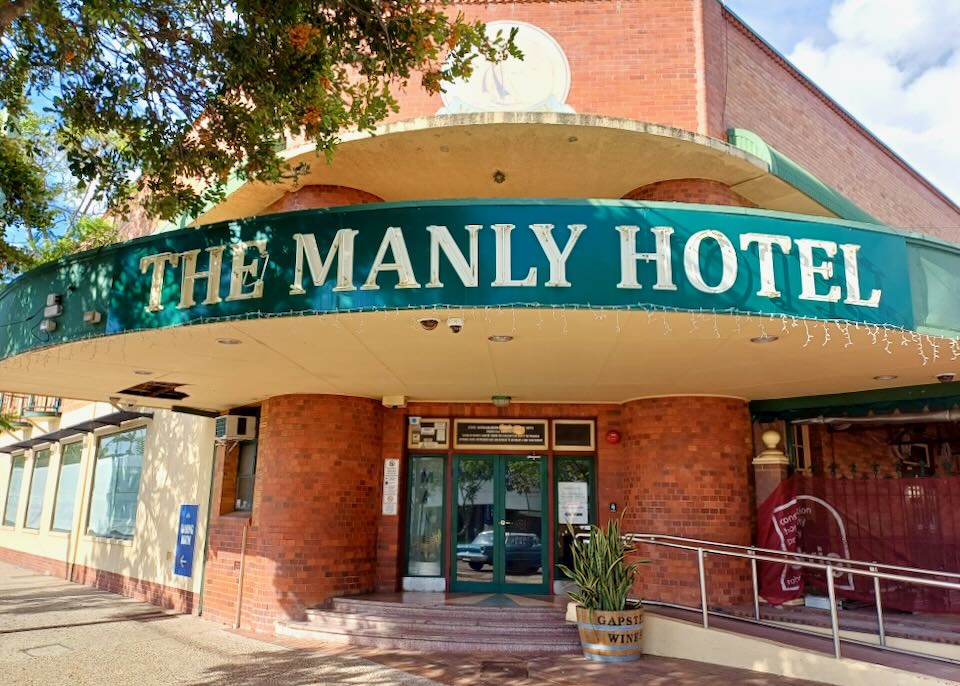 A sign outside a red brick building reads, "The Manly Hotel."