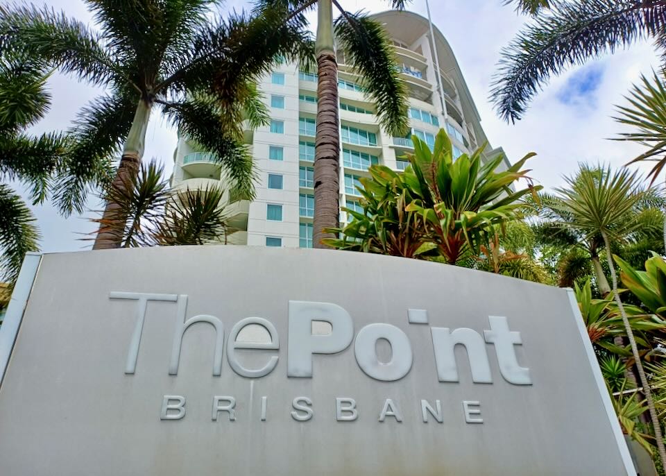 A large sign that reads "The Point Brisbane" in front of a tall palm tree and hotel building.