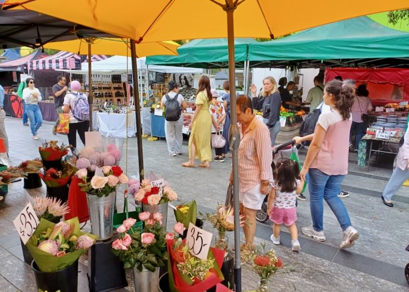 People stand around flowers sold at a market.