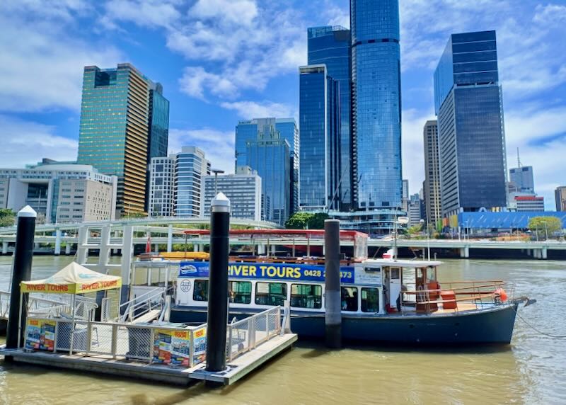 A boat sits on the river by a dock where passengers board.