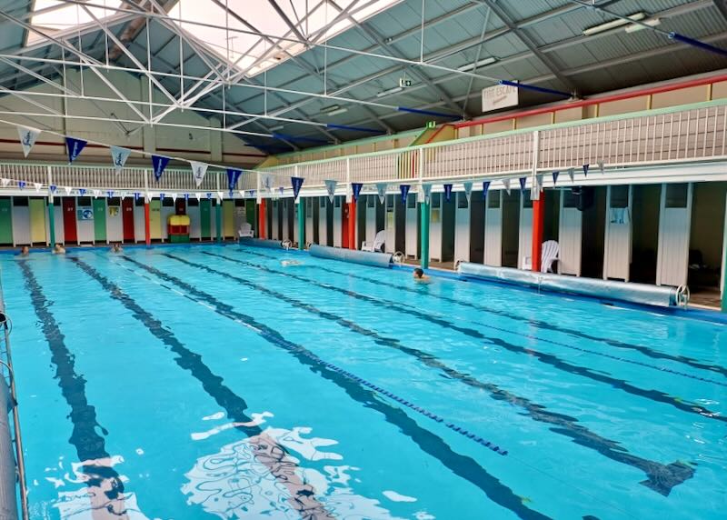 A long indoor swimming pool with dark blue swim lanes and triangle flags hung across the pool.