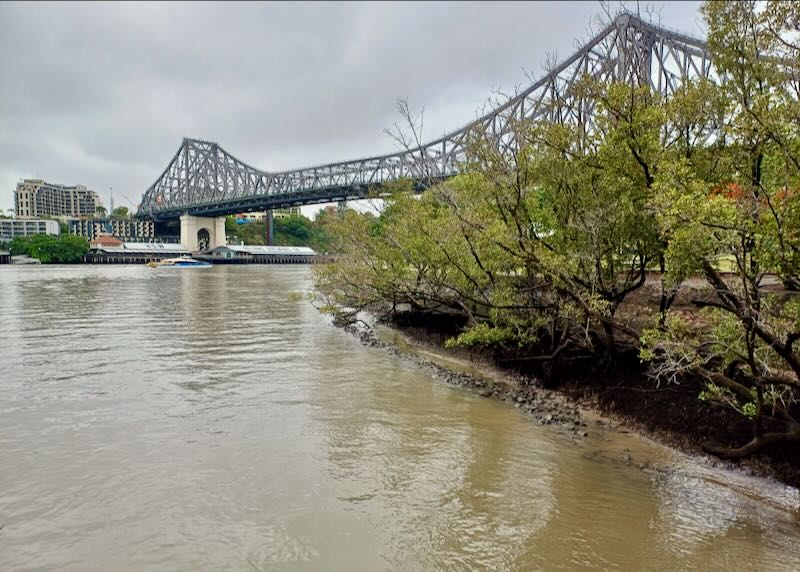 A large two-peaked bridge crosses a brow river.