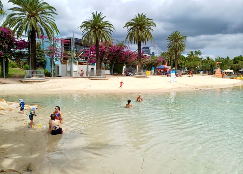 Families sit in shallow water as their children play.