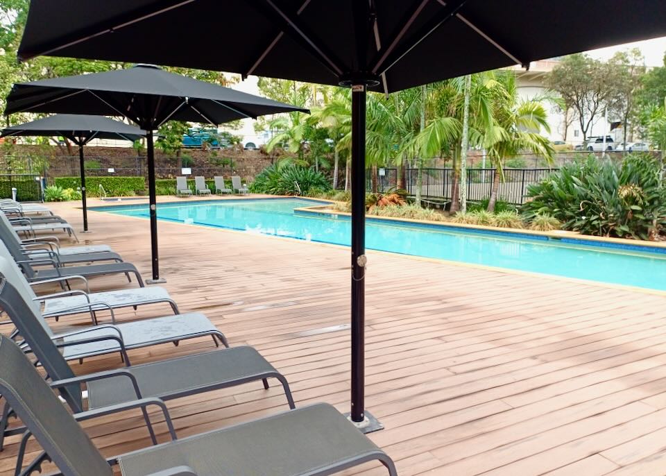 Gray lounge chairs sit under black umbrellas but a light blue pool.