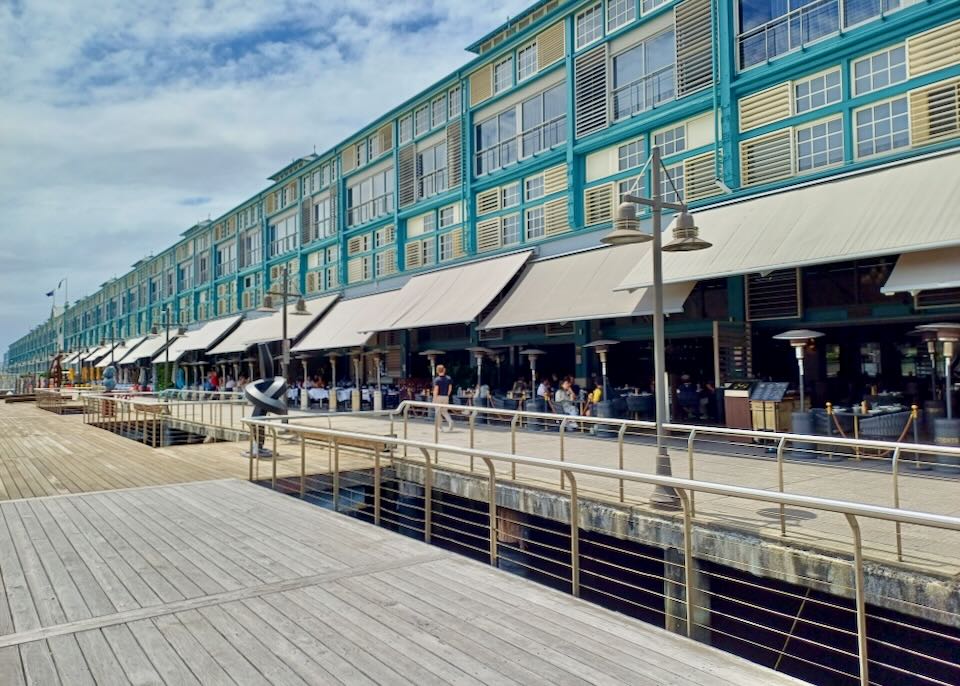 A long pier holds a teal and pale yellow painted multi-level hotel.