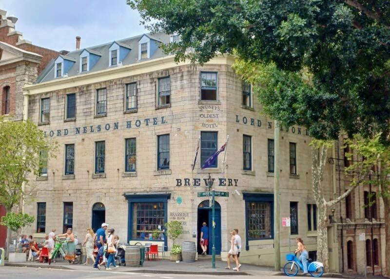 People walk on sidewalks next to an old brewery.