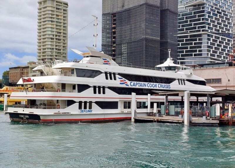 A small harbor cruise boat sits docked by large buildings.