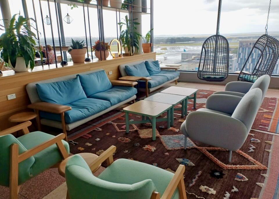 Lounge chairs and sofas sit on a colorful rug with windows overlooking the runway.