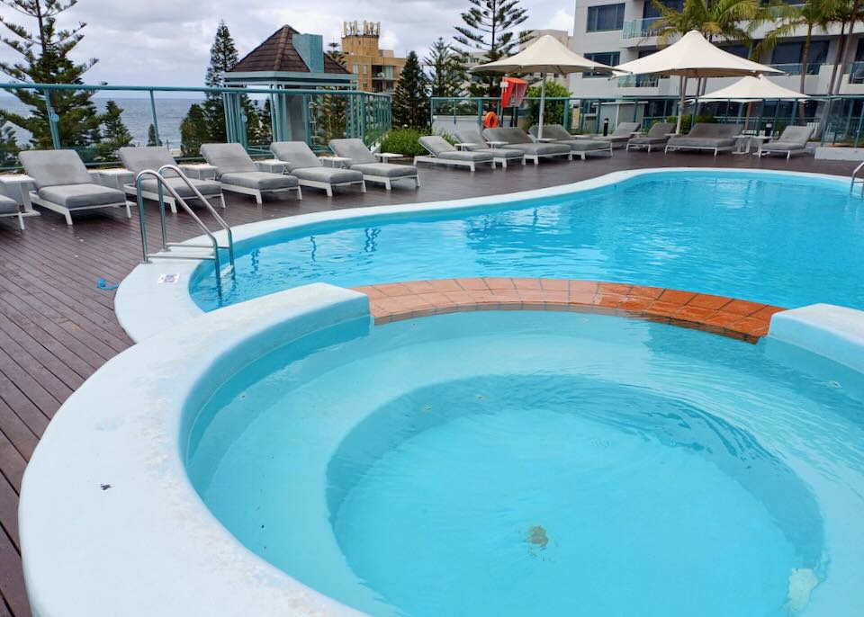 A hot tub shares a wall to an outdoor pool by the sea.