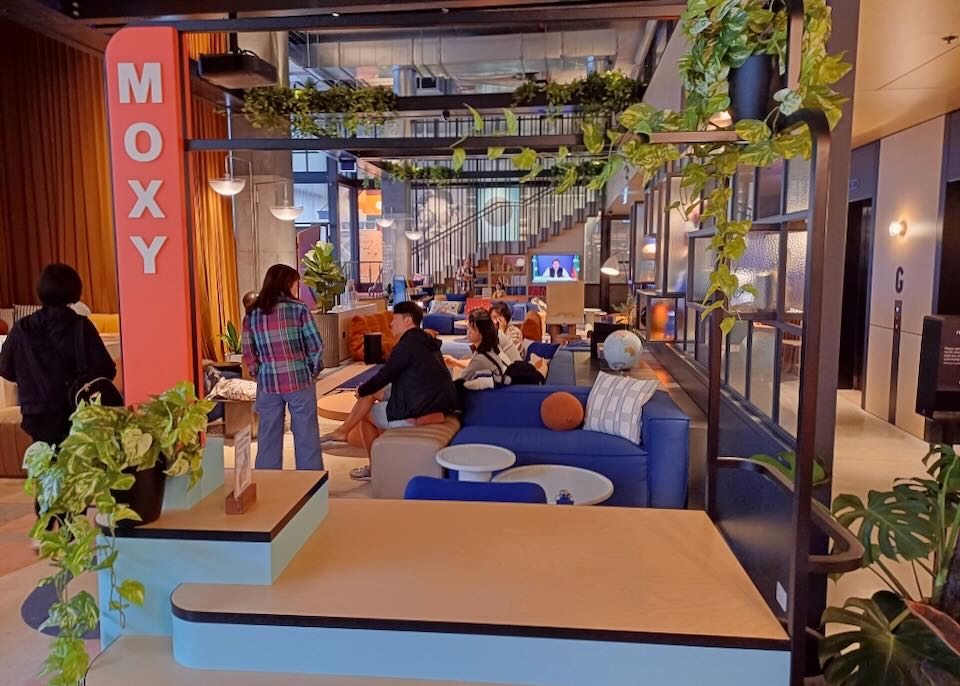 Guests sit on bright blue sofas with orange pillows in a hotel lobby.