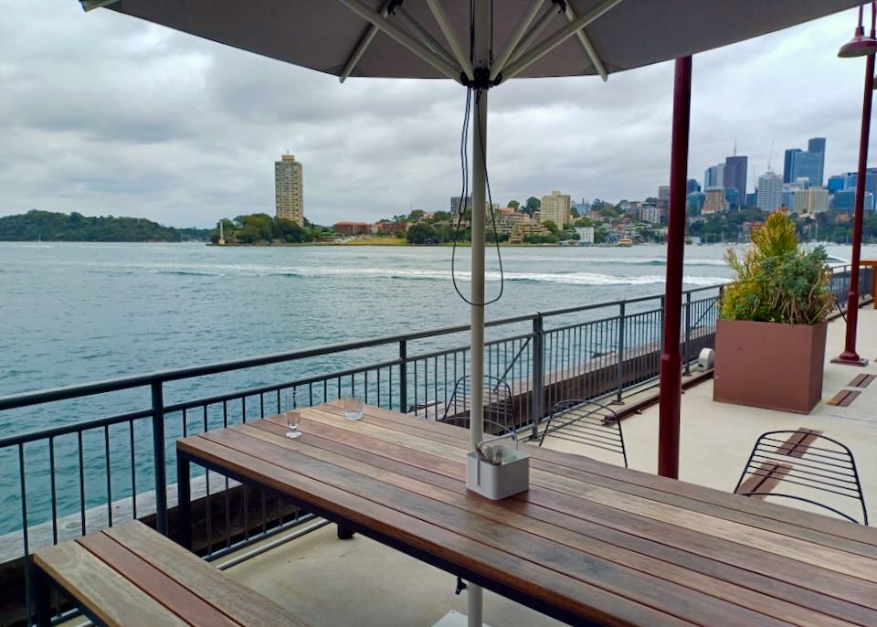 A wood table on a pier has views of water and a city skyline.