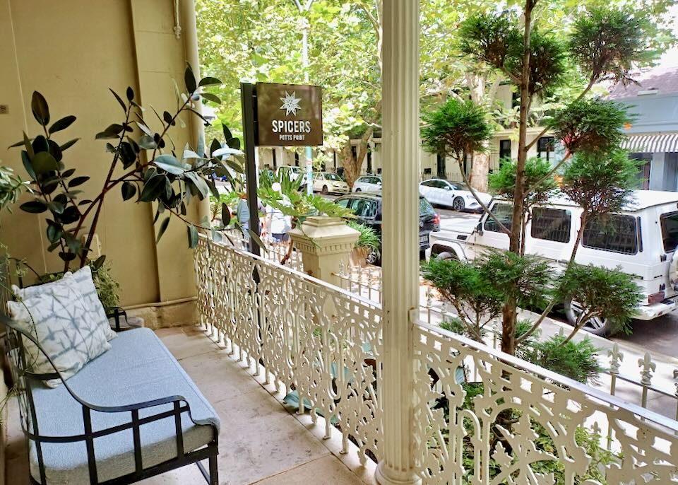 A bench sits on a balcony behind a white painted wrought-iron fence.