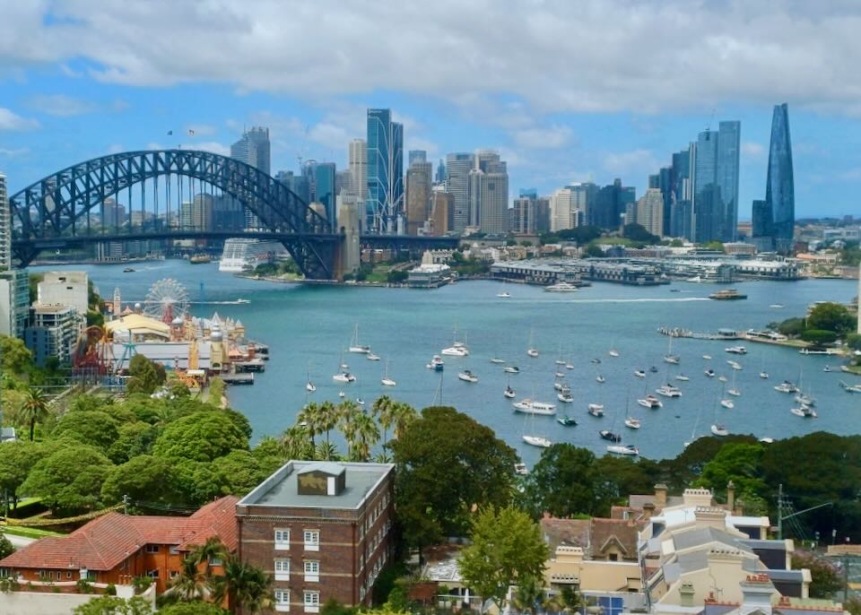 A view of water, buildings, a bridge, and boats sitting in a harbor.