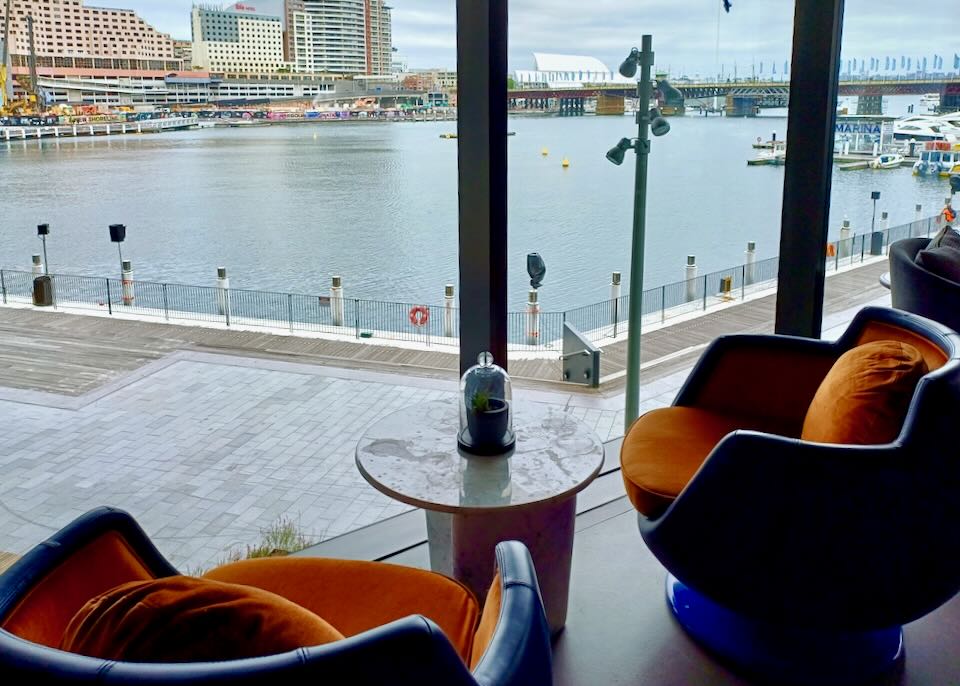 Two velvet blue and orange swivel chairs sit by a window of the harbor.